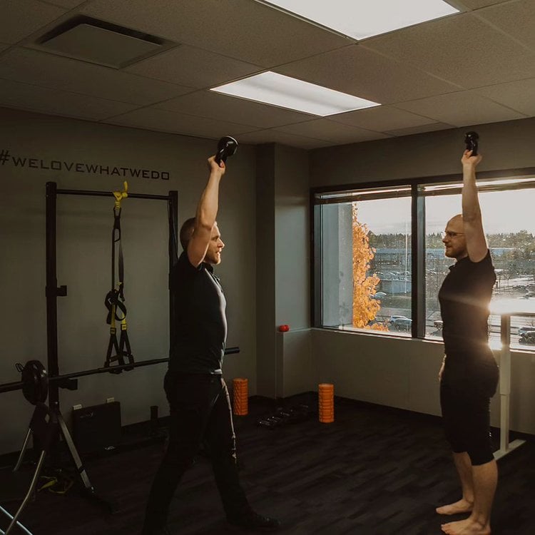 Two clients performing kettlebell rehabilitation exercises in the Pro Motion Calgary movement studio